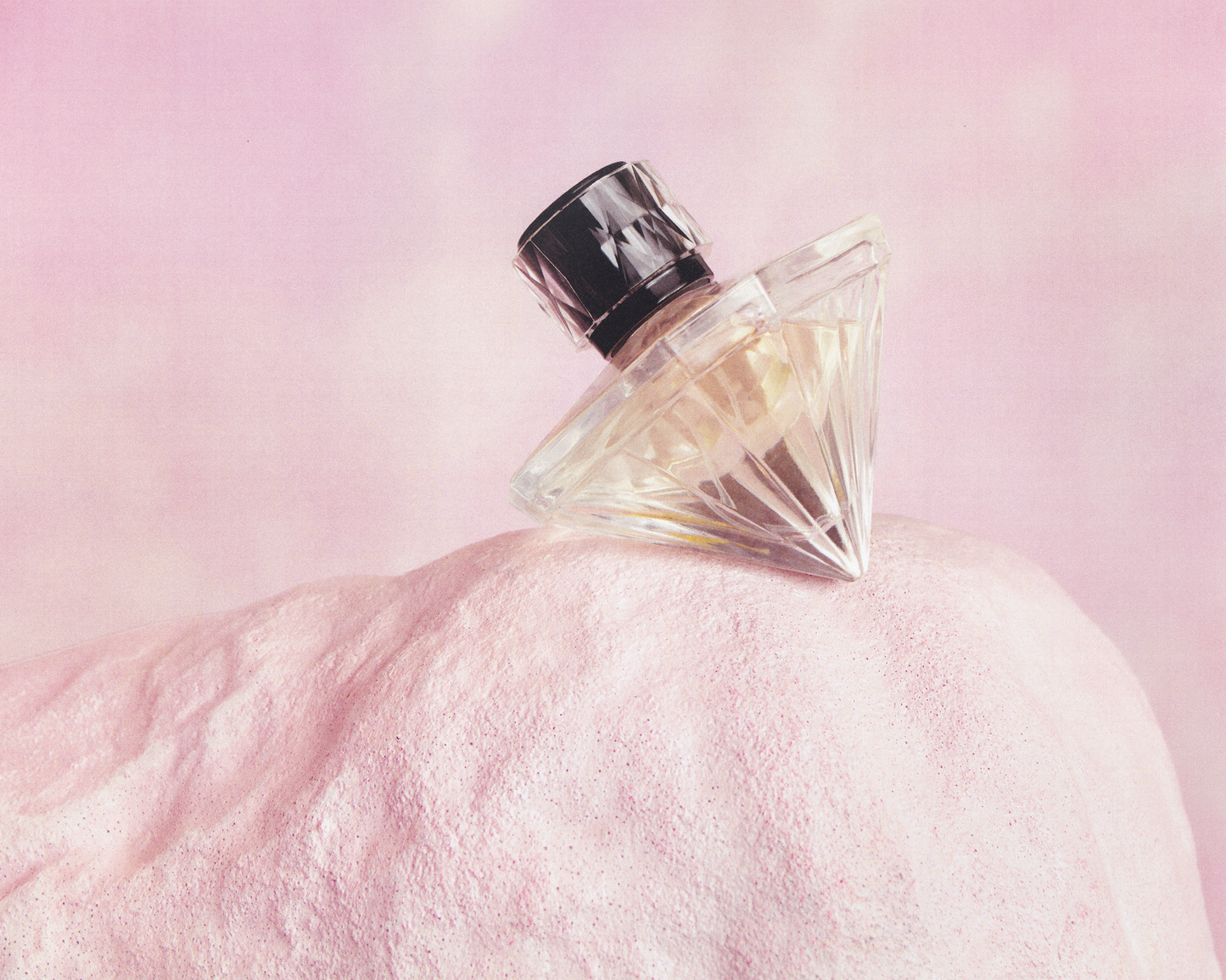 Perfume bottle on a pink textured surface with a soft pink background